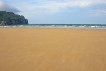 Fototapeta na wymiar Playa vacía con el mar y acantilados al fondo
