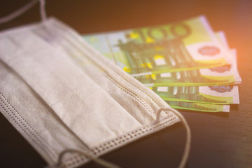 Obraz premium A medical mask on some 100 euro bills . Selective focus. concept of high prices for medical equipment or masks during a pandemic of the coronavirus COVID-19.