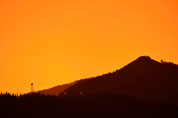 Silueta de un monte y una torre sobre un cielo anaranjado