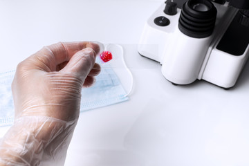 Scientist hand with gloves with blood sample on glass slide next to microscope and medical masks on laboratory table. Concept investigating vaccine against.