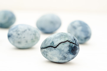 Five blue marble eggs similar to dragon eggs, one of them with a crack, painted in hibiscus tea, lie on a white background, for a card with copyspace