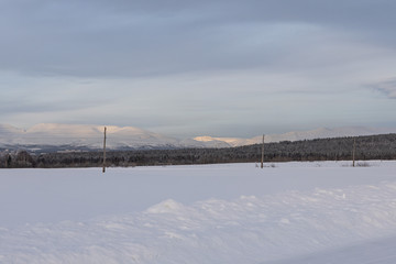 Winter landscape - snow-covered field, forest and mountains in the background. Russian North