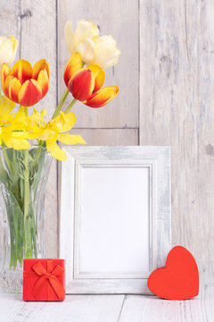 Tulip flower in glass vase with picture frame decor on wooden table background wall at home, close up, Mother's Day design concept.