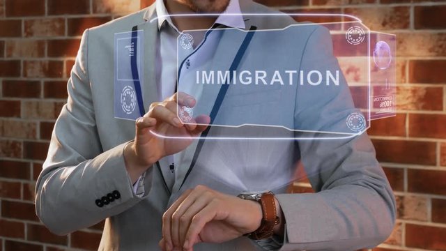 Unrecognizable businessman activates conceptual HUD holograms on smartwatch with text Immigration. Man in jacket with holographic technology on wristwatch on background of brick wall