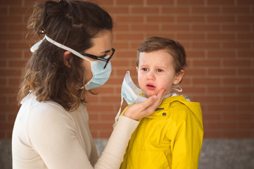 Mother putting face mask on her sad kid during coronavirus and flu outbreak