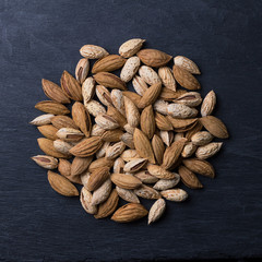 Variety of almonds, mountain and garden on black slate background. top view, square