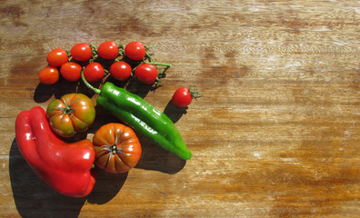 Vegetables illuminated by bright sunlight on an old wooden table. Red and green paprika, tomatoes, tomatoes-cherry. Healthy food. Copy space.