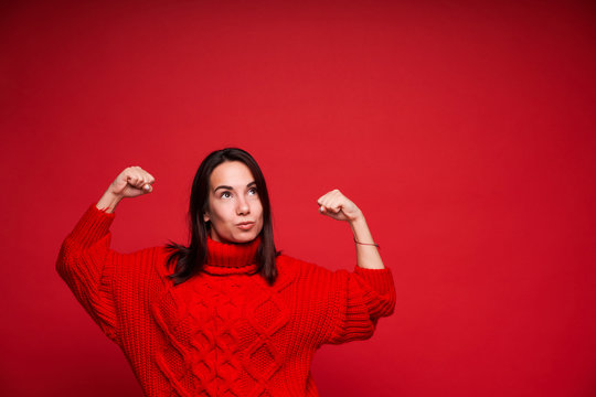 Happy successful young woman with raised arms celebrating success on red background
