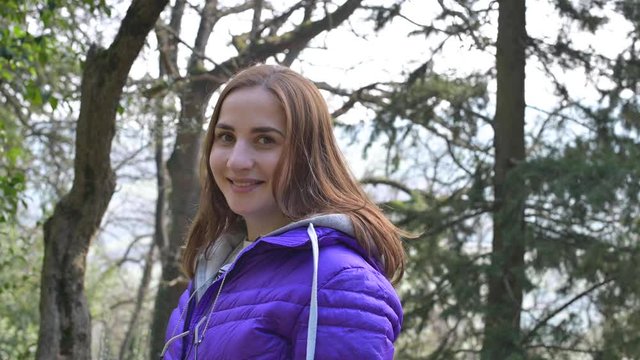 Girl in the park in spring. A young woman in a purple jacket and brown hair is smiling and happy.