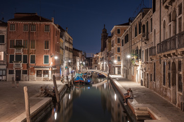 Narrow canal with boats and vintage houses at dusk. Venice city at night
