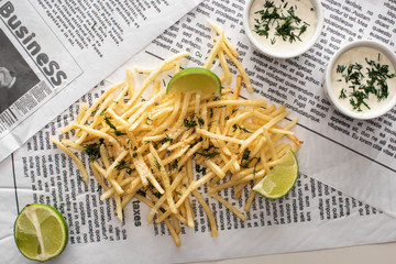 top view of fried french fries, garlic sauce and sliced lime on newspaper