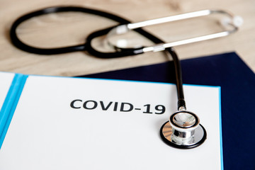Teczka z napisem COVID-19 oraz stetoskop, głowica na kartce z napisem, przyrządy lekarskie
