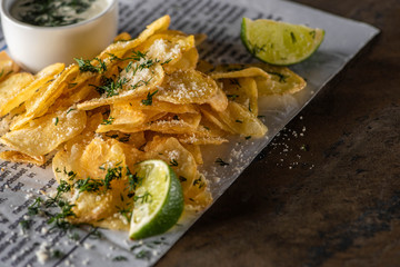 selective focus of potato chips with salt near sliced lime, garlic sauce and newspaper on marble surface