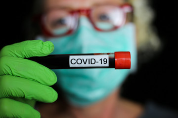 Corona virus diagnostic test concept:  closeup portrait of isolated blonde woman with surgical protection mask and green gloves holding blood vial