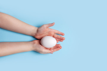 Fototapeta na wymiar White chicken egg in the hands of a child on a blue background. Easter concept.