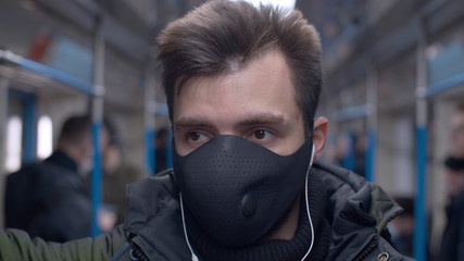 Close up portrait of a young man in a reusable protective mask in subway train. Coronavirus...