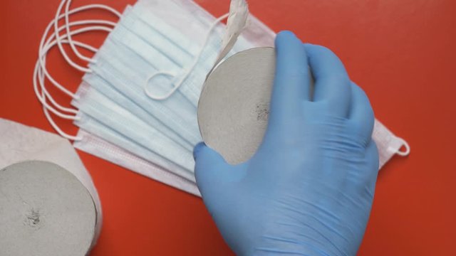 Doctor showing rolls toilet paper on background antiviral face masks and red color backdrop. Human hand protected by blue medical gloves. Lavatory paper - concept fight against coronavirus, hygiene