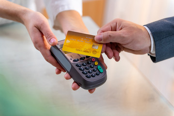 Closeup of caucasian right hand, holding gold credit card on a PIN PAD held by a woman's hands