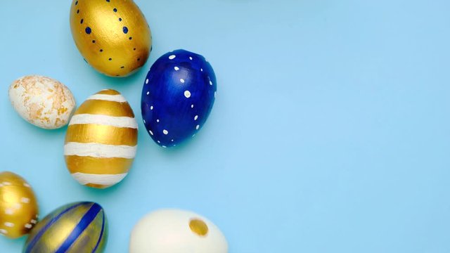 Easter eggs are rolling, knocking each other on blue table. Eggs trendy colored classic blue, white and golden . Happy Easter. Minimal style. Top view.