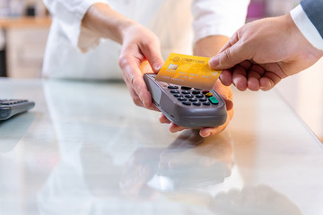 Closeup of caucasian right hand, holding gold credit card on a PIN PAD held by a woman's hands