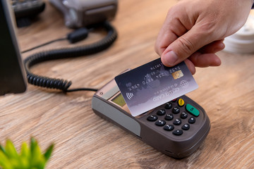 Closeup of Caucasian right hand, holding a black credit card on a POS terminal