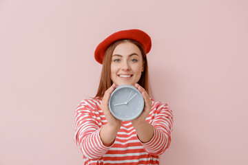 Beautiful young woman with alarm clock on color background