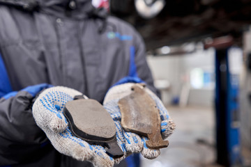 The mechanic holds the old and new brake pads in his hand. Change the old to new brake disc on car in a garage. Auto repair concept.