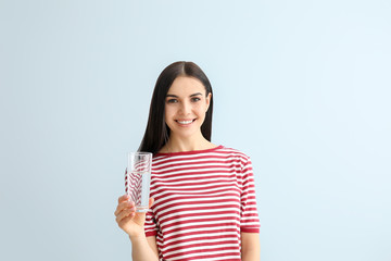 Beautiful young woman drinking water on color background