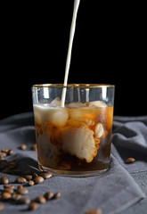 Pouring of milk into cold coffee in glass on table