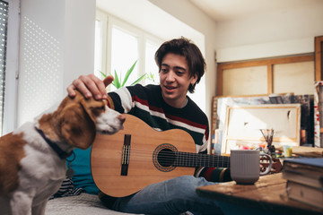 young man playing guitar at home, playing with his dog