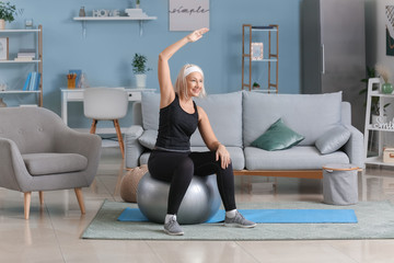 Obraz premium Sportowa dojrzała kobieta robi ćwiczenia z piłką fitness w domu