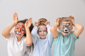 Funny children with face painting on light background