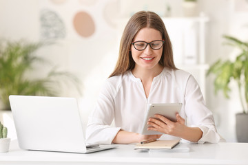 Portrait of beautiful young businesswoman with tablet computer at table in office