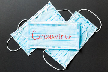 Epidemic background made of coronavirus word on heap of protective medical masks on black...