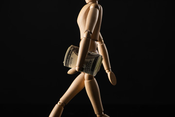 Wooden doll imitating walking with dollar banknotes isolated on black