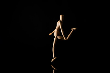 Obraz na płótnie Canvas Wooden doll imitating raising leg on black background