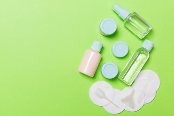 Group of small bottles for travelling on green background. Copy space for your ideas. Flat lay composition of cosmetic products. Top view of cream containers with cotton pads