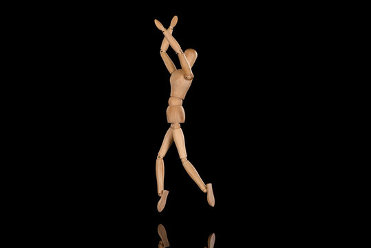 Wooden doll imitating dancing with crossed arms on black