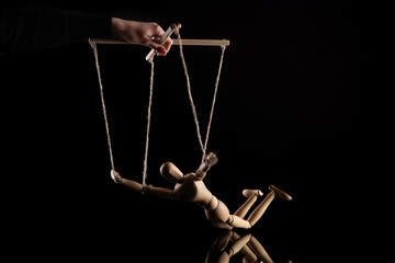 Cropped view of puppeteer holding wooden doll with ropes on black