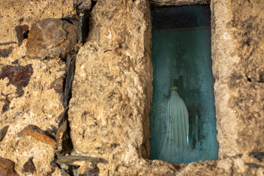 Statuette of the Virgin Mary in a small window of a medieval church on the background of masonry.  Back view.