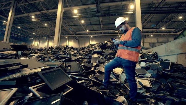 A pile of broken monitors and a male worker standing on it. Garbage, waste, trash recycling center.