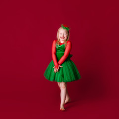 Little blonde girl in a christmas and new year green costume having fun on red background. Space for text. Dreams come true Merry Christmas