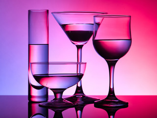 Different glass goblets on a red and purple background. Beautiful still life