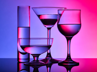 Different glass goblets on a red and purple background. Beautiful still life