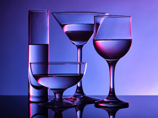 Different glass goblets on a and purple background. Beautiful still life