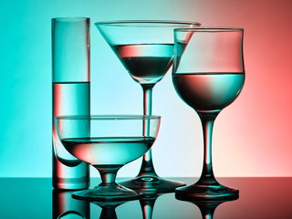 Different glass goblets on a turquoise and orange background. Beautiful still life