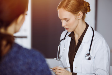 Cheerful smiling female doctor and patient woman discussing current health examination while...