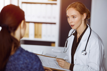 Cheerful smiling female doctor and patient woman discussing current health examination while...