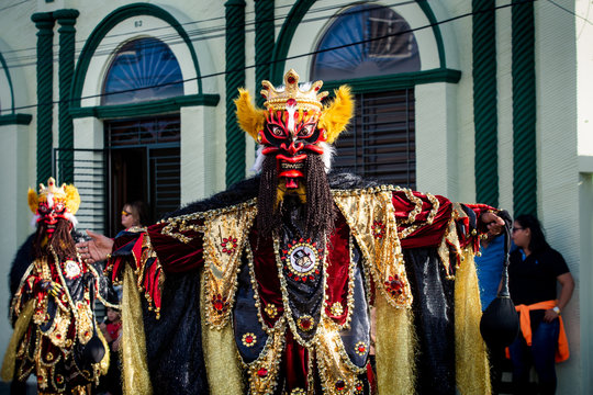 tall man in flamboyant costume pose for photo on city street at dominican carnival