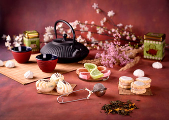 Chinese or Jananese teapot with cups, tea, cakes and flower on dark red background